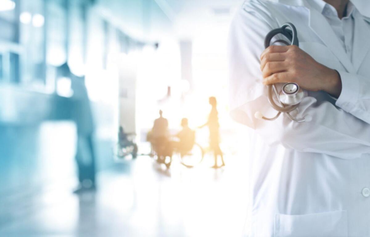 Doctor in white coat with stethoscope in forefront with patients in background