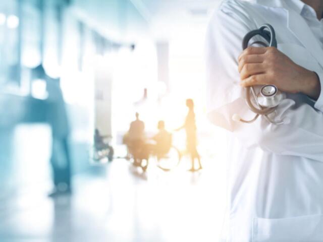 Doctor in white coat with stethoscope in forefront with patients in background